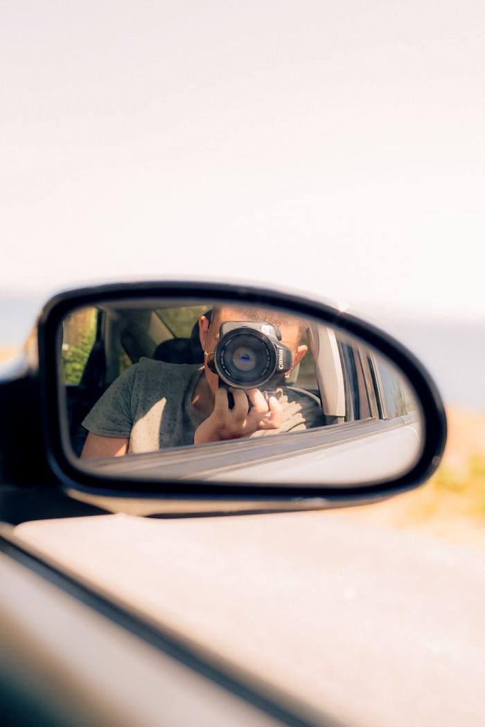 Photographer capturing a moment through car mirror reflection on a sunny day.